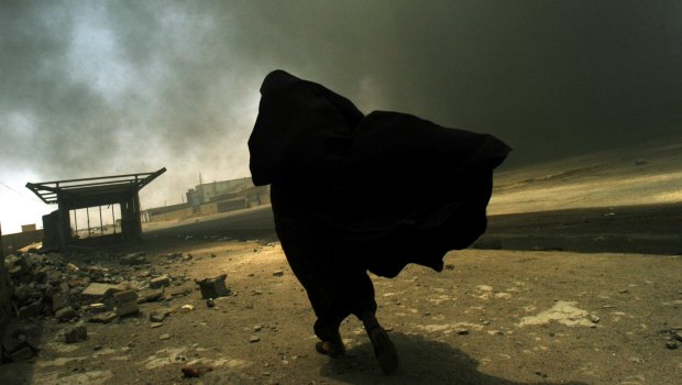 An Iraqi woman walks through a plume of smoke rising from a massive fire.