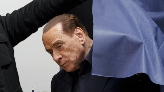 Italian former premier and leader of Forza Italia party Silvio Berlusconi holds his ballot as he is helped get out of a polling booth, in Milan.