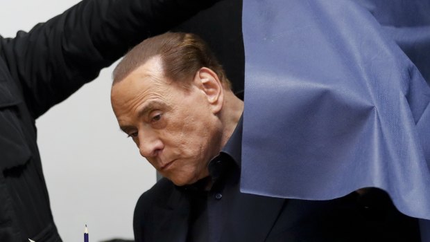 Italian former premier and leader of Forza Italia party Silvio Berlusconi holds his ballot as he is helped get out of a polling booth, in Milan.