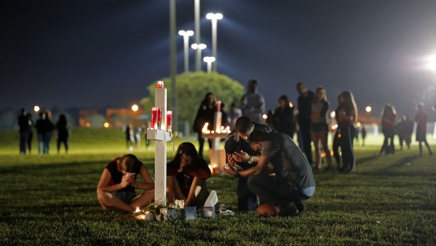 People pray around one of seventeen crosses, after a candlelight vigil for the victims of the Wednesday shooting at Marjory Stoneman Douglas High School, in Parkland, Florida.