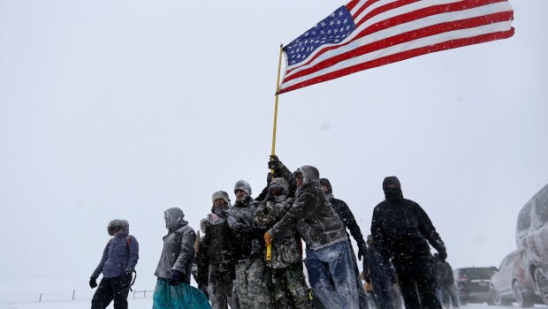 Military veterans huddle together to hold a United States flag against strong winds during a march to a closed bridge outside the Oceti Sakowin camp to protest the Dakota Access oil pipeline in Cannon Ball, ND.