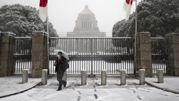 Snow falls as a man holding an umbrella walks past the main gate to the National Diet building in Tokyo.