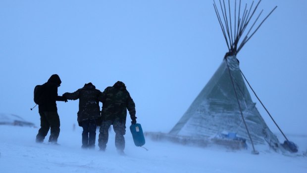 People walk along a snowy hillside in a storm at the Oceti Sakowin camp where people have gathered to protest the Dakota Access oil pipeline in Cannon Ball, ND.