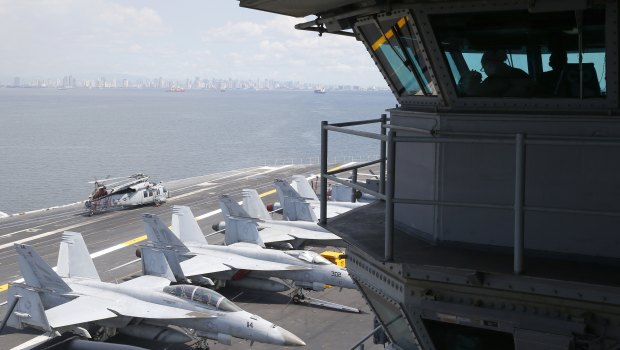 US Navy officers operate on the flight deck control tower as military aircraft sit on the flight deck of the USS Carl Vinson.