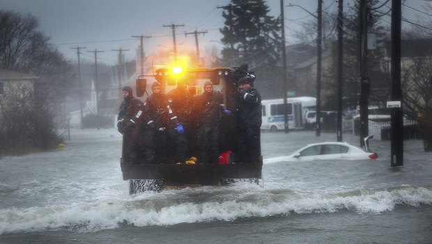 A Marine dive team is transported along a flooded Sea Street, Boston, by front-end loader on Friday.