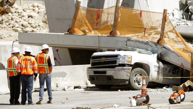 Workers stand next to a section of the collapsed pedestrian bridge in Florida.
