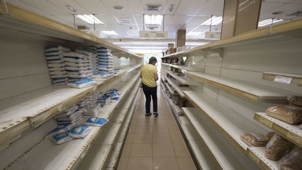 A customer moves along empty shelves as she shops for groceries at a supermarket in Caracas, Venezuela.