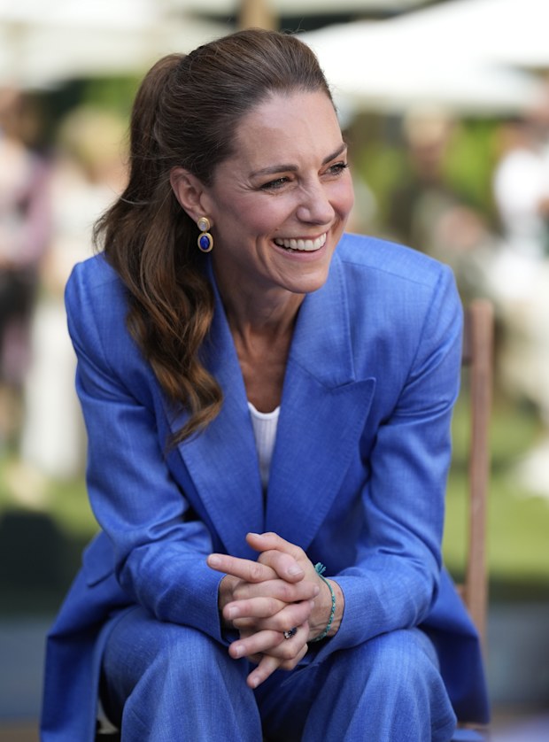 Catherine, Princess of Wales sits leaning forward with her elbows on her knees, wearing a bright blue suit.