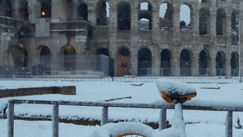 A bicycle is parked in front the ancient Colosseum during a snowfall in Rome.