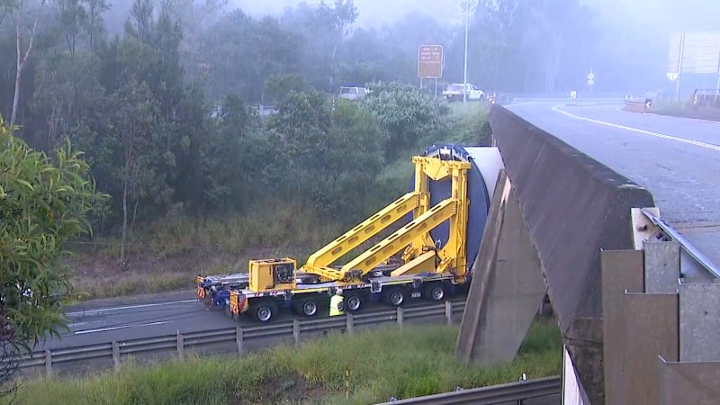 Truck carrying wind turbine stuck under road bridge