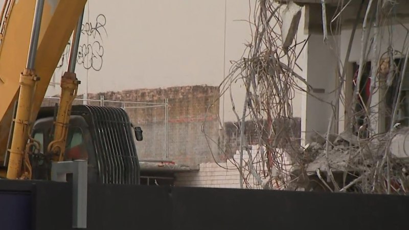 Man in excavator holding up partially collapsed building