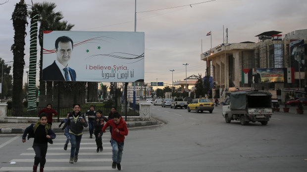 Syrian children cross an Aleppo street in front of a billboard of President Bashar al-Assad. A new report says Assad's chemical attacks on Syrians may have been enabled by North Korea. 
