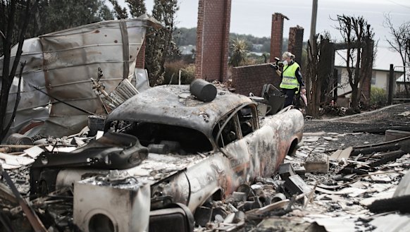 A police officer takes photos of the aftermath of the Tathra bushfire.