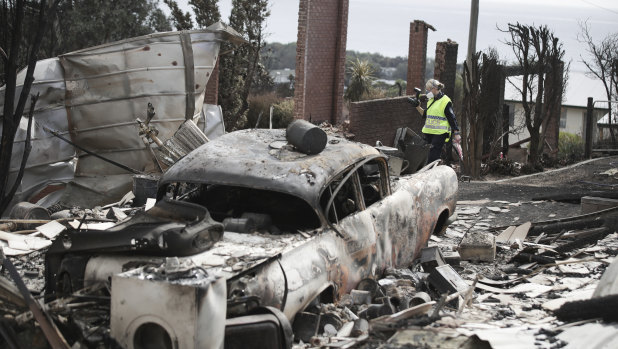 A police officer takes photos of the aftermath of the Tathra bushfire.