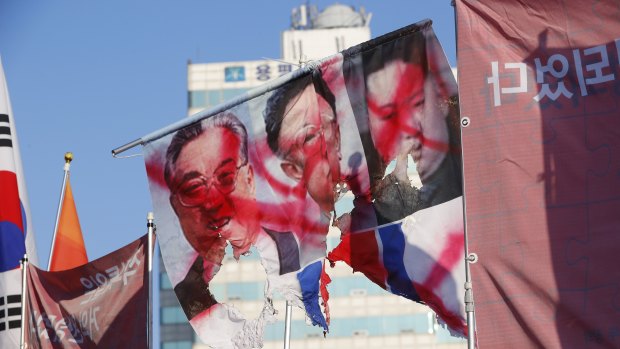 A ripped flag with the portraits of late North Korean leaders, from left, Kim Il-sung, Kim Jong-il and current leader Kim Jong-un during a pro-US, anti-North Korea rally near the Pyeongchang Olympic Stadium.