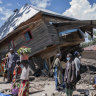 People walk next to a house destroyed by the floods in the village of Nyamukubi, South Kivu province, in Congo.
