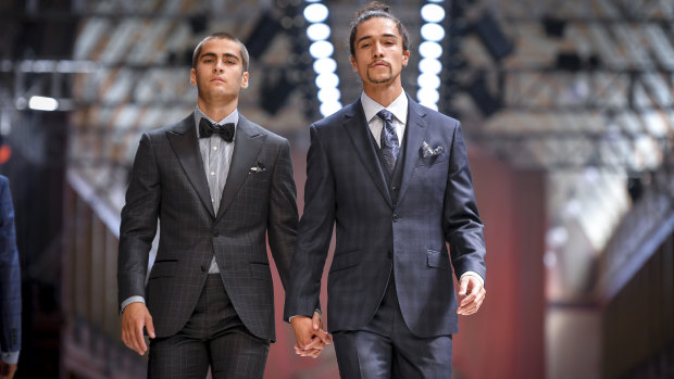 Two male models dressed as grooms hold hands at rehearsals for the bridal runway at Melbourne Fashion Festival.