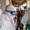 Health workers wearing protective suits prepare for Ebola response operations as residents gather outside a hospital in Mongbwalu, Democratic Republic of the Congo.