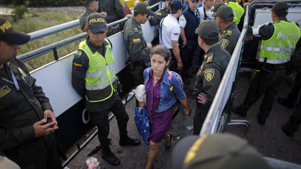 Police stand guard as a Venezuelan woman crosses into Colombia through the Simon Bolivar bridge linking San Antonio del Tachira, Venezuela, with Cucuta, Colombia.