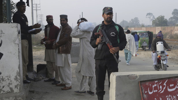 A police officer stands guard while another taking information visitors at a checkpoint of a prison, where the trial of a serial killer is being held, in Lahore, Pakistan.