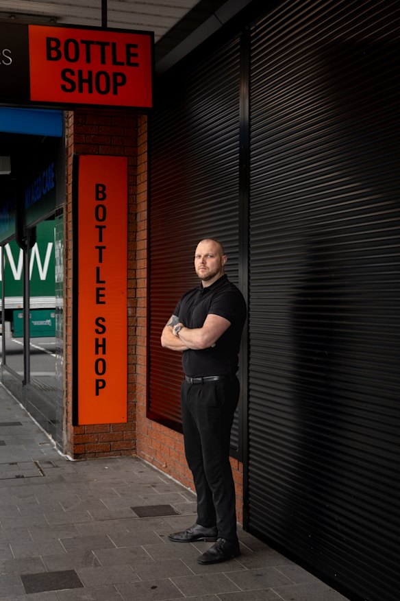 Chris Thompson outside his bottle shop with its shutter down.