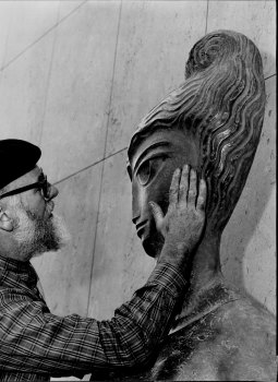 Sculptor Tom Bass puts the finishing touches to his modern version of the AMP emblem, in copper, on the new building. February 7, 1962.