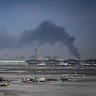 A plume of smoke caused by an Iranian strike is seen in the background as Emirates planes are parked at Dubai International Airport on Sunday.