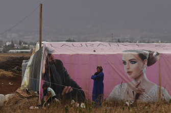A woman stands in front of a temporary shelter as she watches children playing in an unofficial camp in the Bekaa Valley in Lebanon.