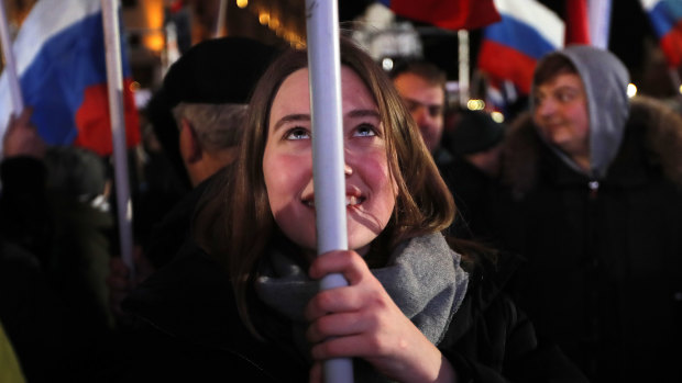People wave Russian flags as they wait for election results in Manezhnaya square, near the Kremlin, in Moscow on Sunday.