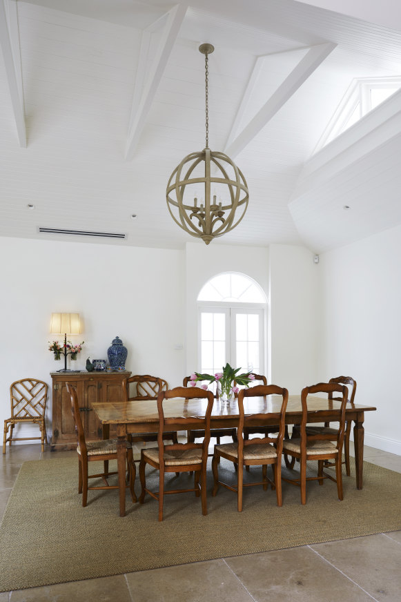 The dining room features a large Cromwell furniture orb pendant and an antique French refrigerator cabinet. Arched double doors lead to the conservatory.