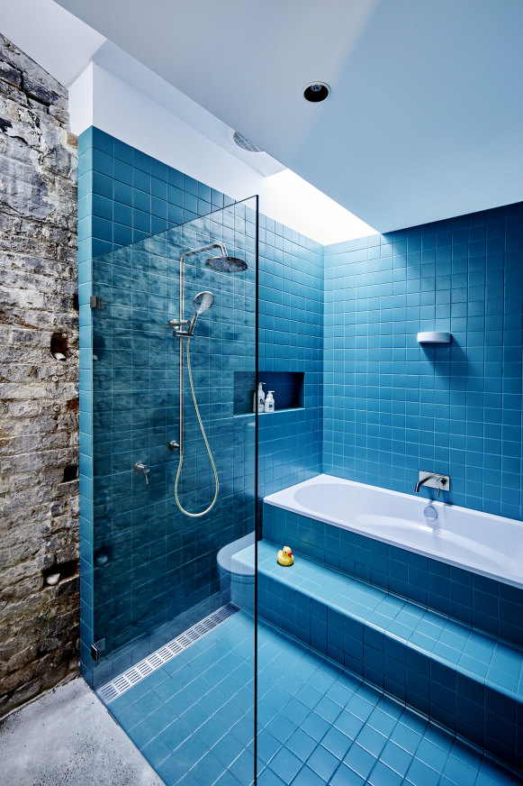 A doorway from the kitchen leads to a family bathroom. Part of the original stable wall is exposed, offering a textural contrast to the glossy tiles.