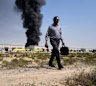 A man walks away after watching a black plume of smoke rising from a warehouse in the industrial area of Sharjah City, United Arab Emirates.
