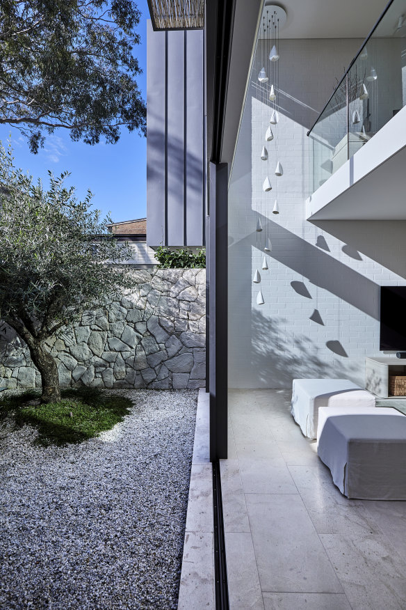 A courtyard leads to a living room with a double-height void extending to an upstairs study. Porcelain pendant light by Bocci, ottomans designed by Freya Salter.