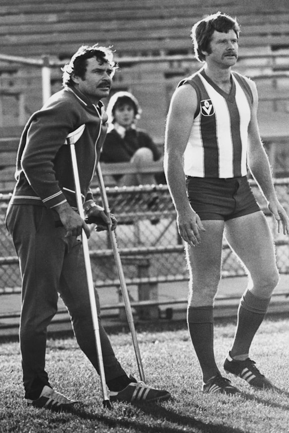 North Melbourne football coach  Barassi, on crutches, takes the team for practice alongside player Barry Davis.