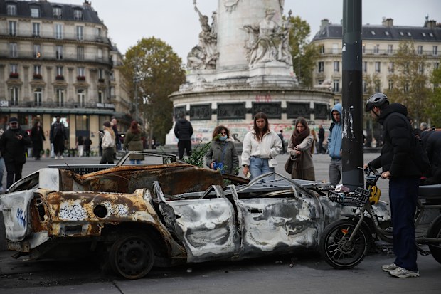 People look at burned-out cars in central Paris after a quiet night on Monday under a curfew.