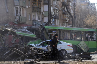 A Ukrainian soldier passes by a destroyed a trolleybus and taxi after a Russian bombing attack in Kyiv. 