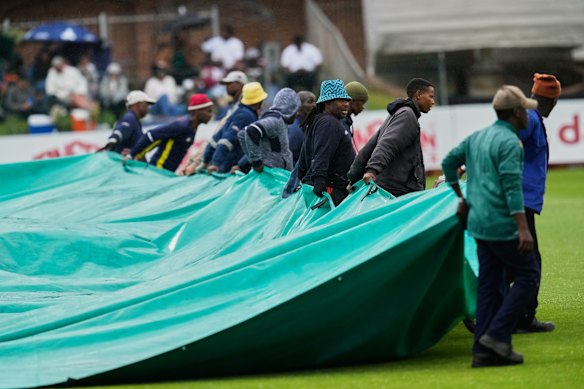 Groundsmen pull the covers as rain delays match on day one. 
