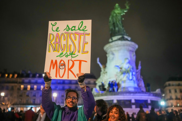 People react during a gathering at Place de la République in Paris after it was announced Jean Marie Le Pen had died. Le Pen founded the French far-right movement in the 1970s. The sign reads “The dirty racist is dead”.