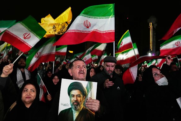 Pro-government supporters wave national flags as one of them holds a picture of the Supreme Leader Ayatollah Mojtaba Khamenei during a rally in a square in western Tehran.