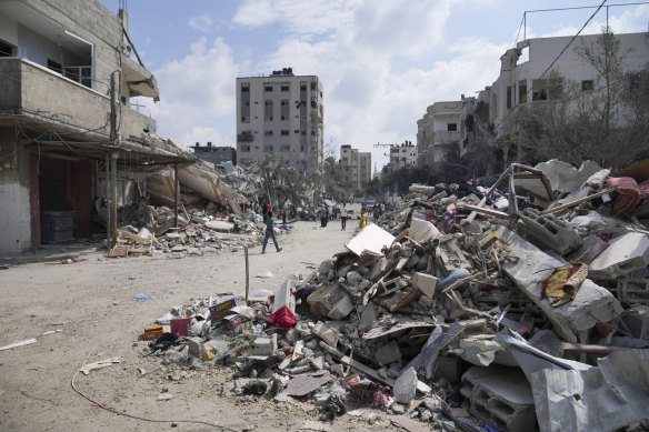 Palestinians walk by buildings destroyed in Israeli airstrikes in Nuseirat camp in central Gaza Strip on Monday.