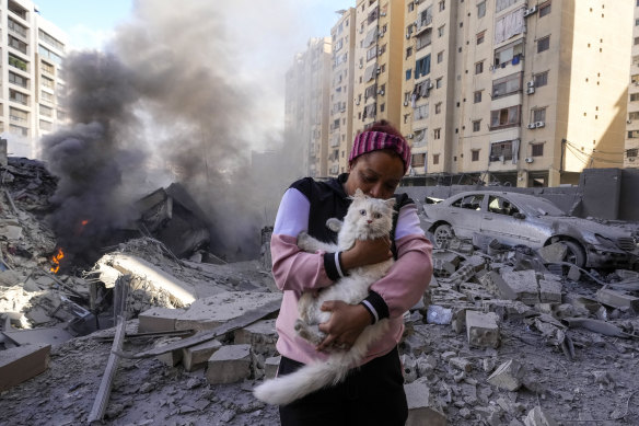 A woman holds her cat in front of a destroyed building at the site of an Israeli airstrike in Dahiyeh, Beirut.