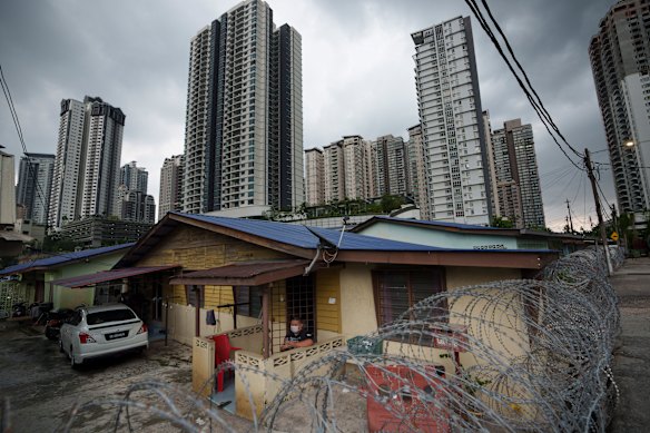 A resident wearing face mask sit outside his house next to barbwire at Segambut Dalam area placed under and enhanced movement control order (EMO).