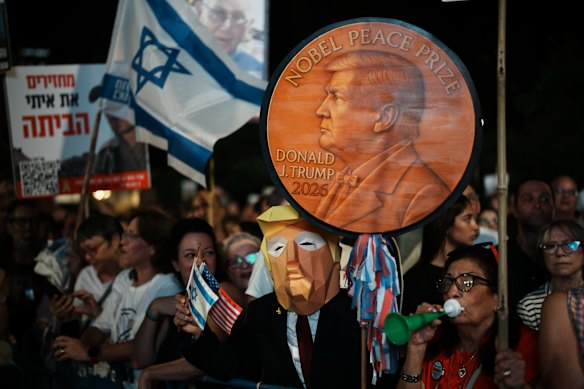 Um homem usando uma máscara de Donald Trump segura uma placa apoiando o presidente dos EUA no Prêmio Nobel da Paz em Tel Aviv.