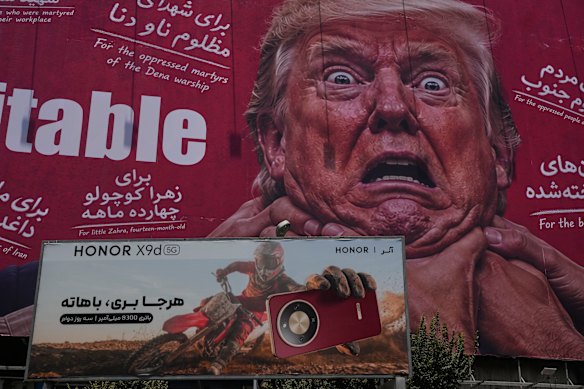 La pubblicità di uno smartphone si trova davanti a un cartellone raffigurante il presidente degli Stati Uniti Donald Trump mentre viene afferrato per il collo a Teheran, in Iran.