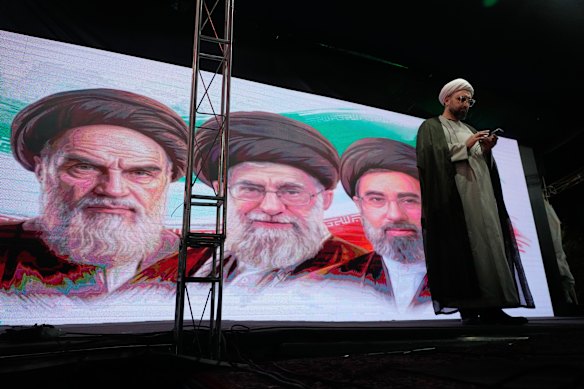 A cleric checks his phone in front of portraits of the late Iranian revolutionary founder Ayatollah Khomeini (left), late Supreme Leader Ayatollah Ali Khamenei (centre) and Supreme Leader Ayatollah Mojtaba Khamenei, during a pro-government gathering in Tehran on Sunday.