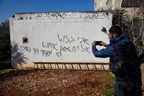 Seorang pria Palestina mengambil gambar grafiti dalam bahasa Ibrani yang dibuat saat pemukim Israel mengamuk di pagi hari dan bertuliskan “Avi Bluth, jangan main-main dengan kami, brigade raja David,” di kota Ein Yabrud, Tepi Barat, pada 17 Desember.