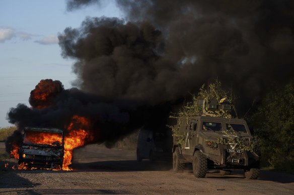 A Ukrainian armoured military vehicle travels past a burned car near the Russian-Ukrainian border.