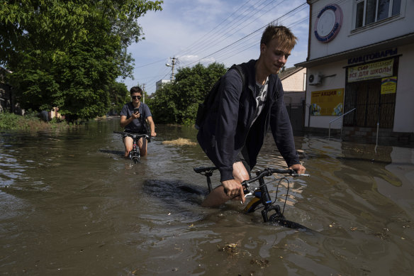 Local residents try to ride their bikes along a flooded road after the Kakhovka dam wall was destroyed in Kherson, Ukraine.