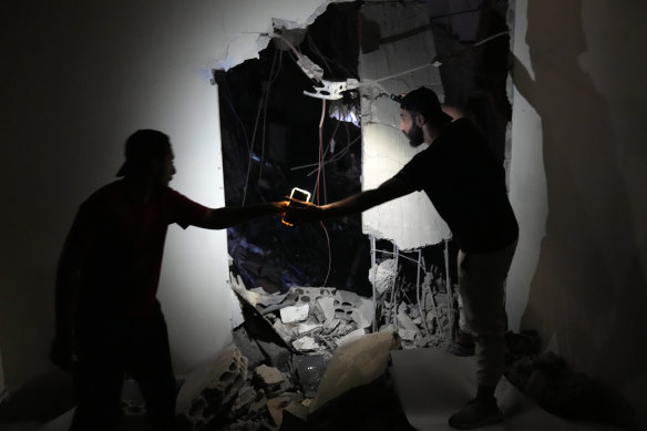 Two men use their phone light, as they check a house on a destroyed building that was hit by an Israeli airstrike in the southern suburbs of Beirut.