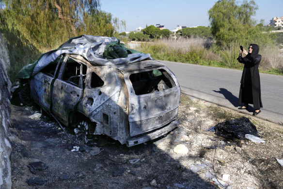 A woman takes photos of a burned and damaged car used by senior Hezbollah leader Wissam al-Tawil, who was killed on Monday in the village of Khirbet Selm in southern Lebanon.